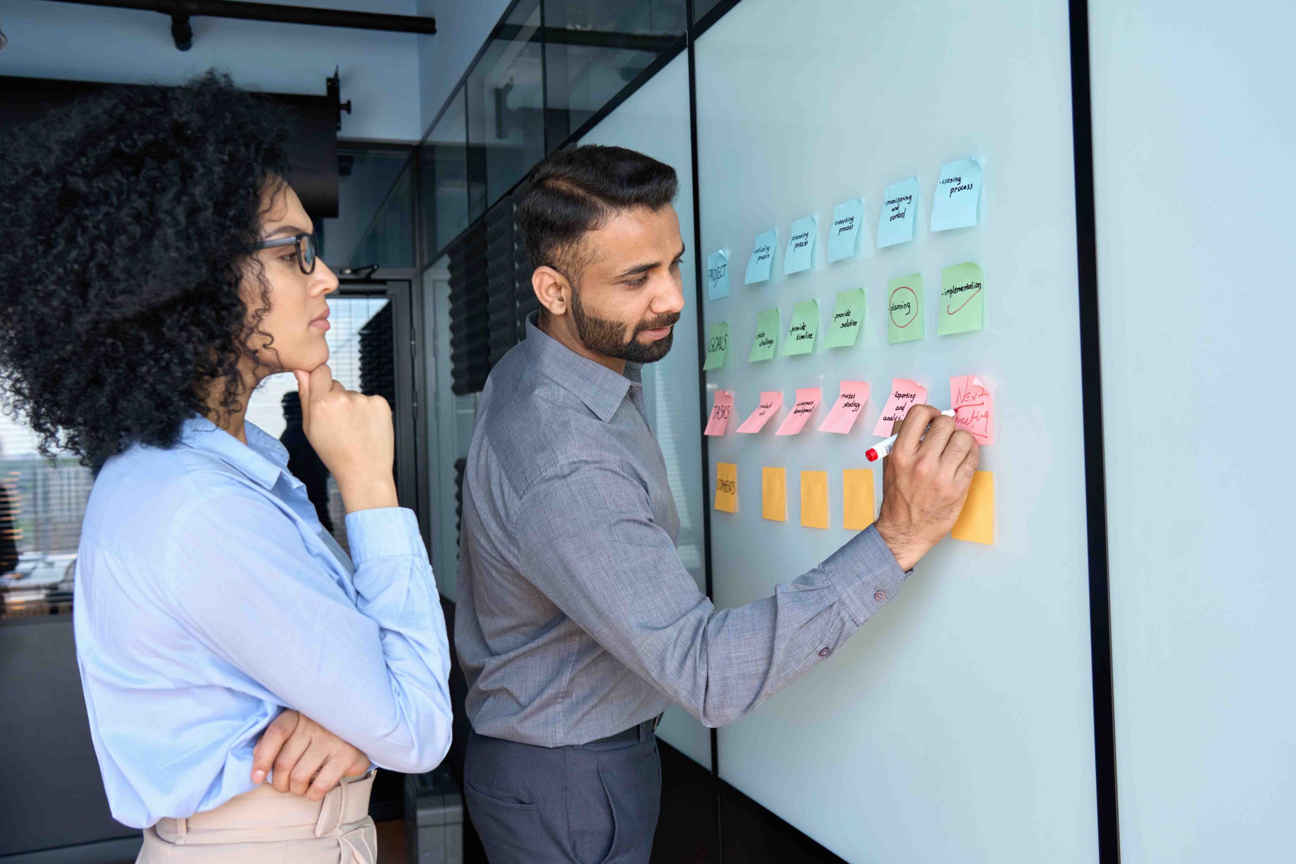 Team members planning project workflow using sticky notes on glass board in modern office setting